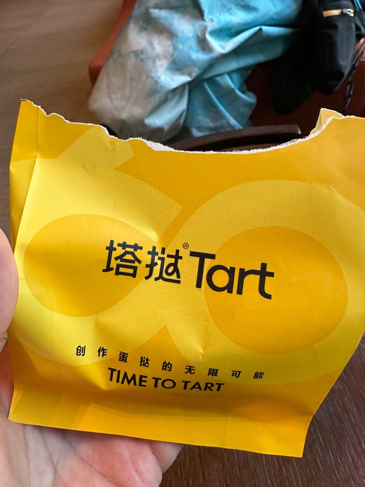 En hand håller en uppriven gul papperspåse från ett kinesiskt bageri med varumärket Tart tryckt på framsidan, beställd och betald i förväg via app.