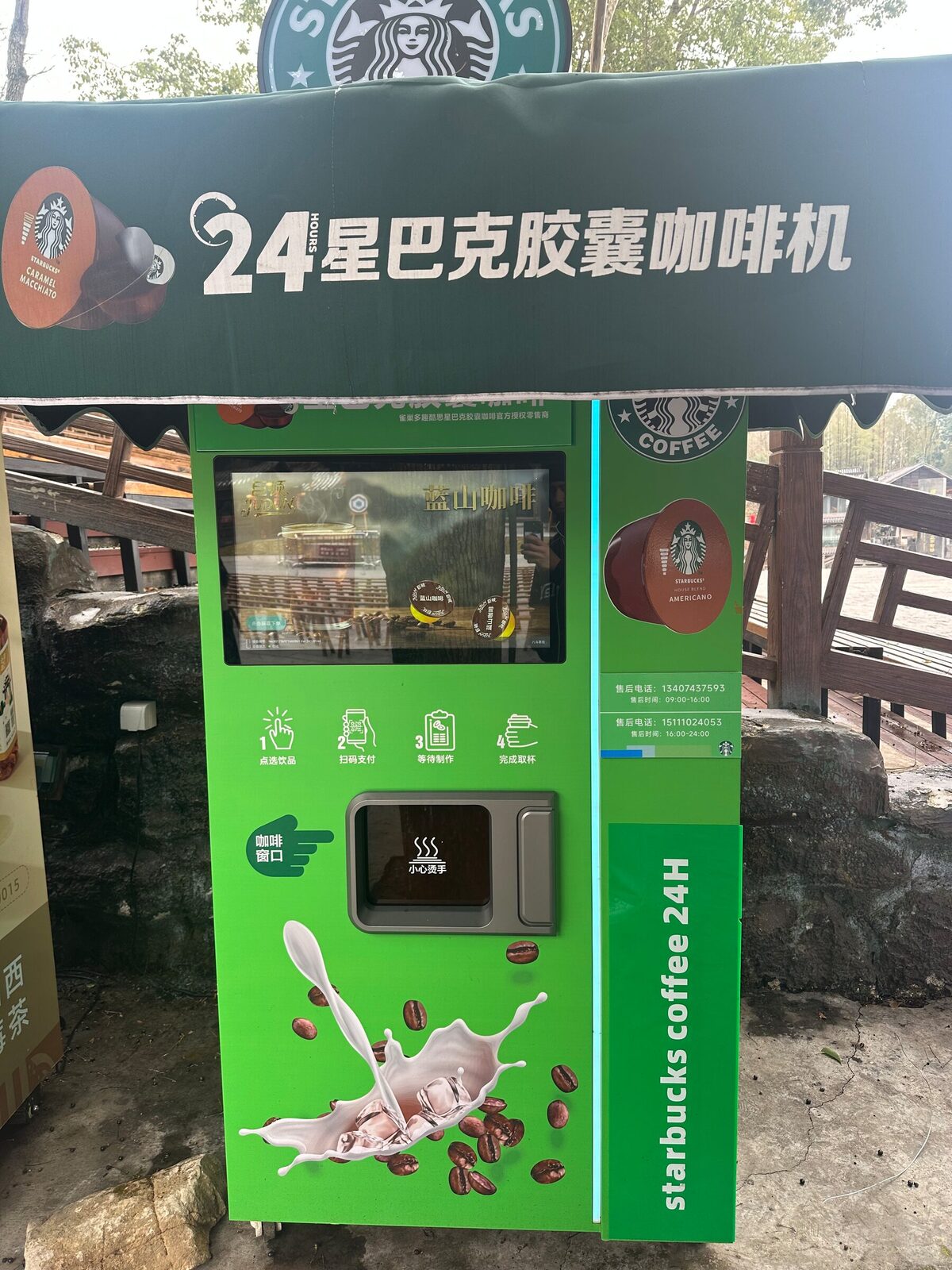 En klargrön kaffeautomat från Starbucks står under ett eget tak vid en stenlagd bergsstig i Xiangxi. Automaten har en pekskärm, en illustrerad instruktion i fyra steg, en utlämningslucka för koppen och texten om kapselkaffe dygnet runt.